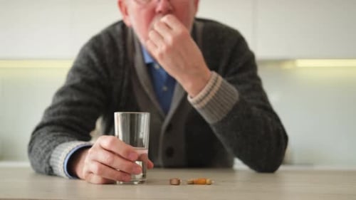 Senior Man Takes Medicine with Water Indoors