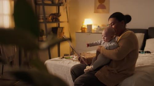 Smiling Black Mother Reading Fairy Tales for Baby Son in Bedroom