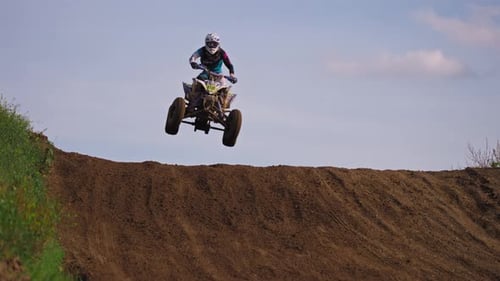 Quad bike race driver jumps over a hill during the race. Dirt coming up while driving past.