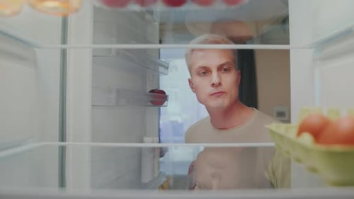 Man Looking Inside Refrigerator at Food Items