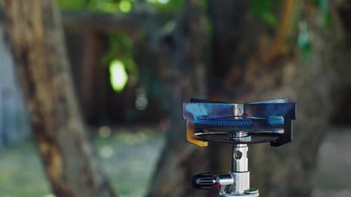 Side view of lighting a camping stove with a match, and then placing a pot on the stove.