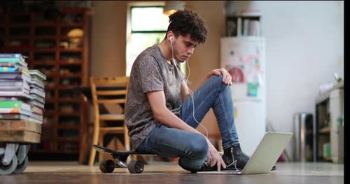 Young Man Using Laptop While Sitting on Skateboard