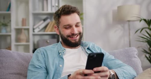 Man Smiling at Phone While Relaxing on Couch