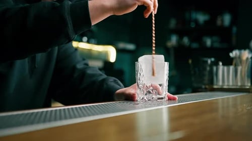 professional bartender stirring ice cubes with a long spoon behind the bar a young man