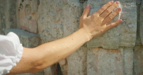 Hand touching ancient carved stone wall of Mayan ruins during tour in Mexico