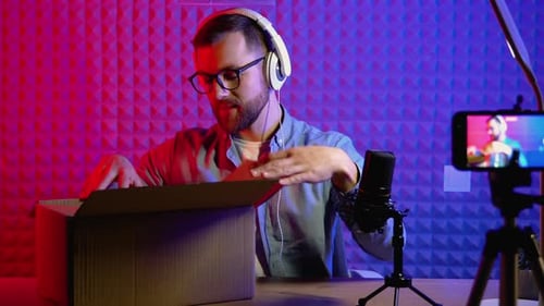 Man Unboxes Merchandise at Desk with Microphone