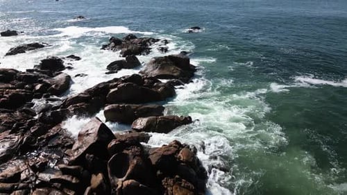 Sparkling Ocean Water Swirling Around Dark Jagged Rocks At Shore