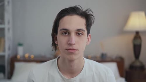 Closeup Portrait of Carefree Young Man Looking at Camera As Pillow Hitting Face in Slow Motion Front