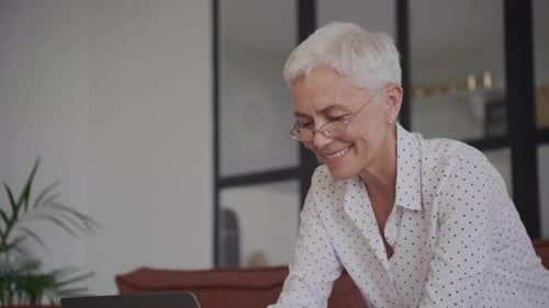 Senior Woman Smiling While Using Laptop At Home