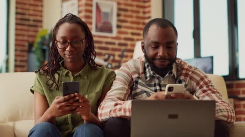 Smiling Couple Using Mobile Phones on Sofa