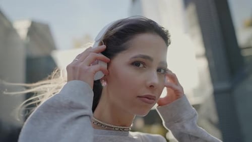 Woman Puts on Wireless Headphones in City