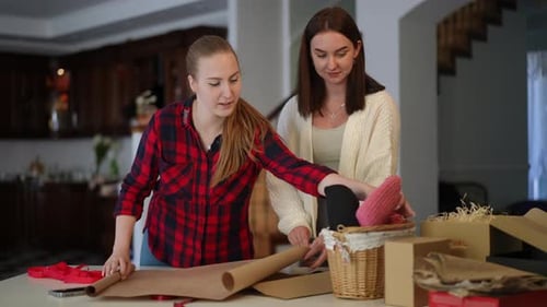Young Women Wrapping Gifts at Table Indoors
