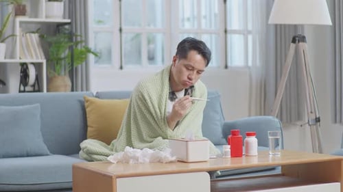 Man Taking Temperature Feeling Sick on Couch