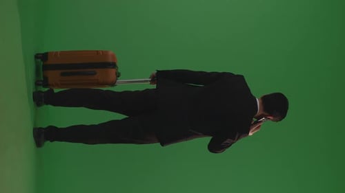 Asian Businessman With Luggage Talking On Smartphone While Walking And Standing In The Green Screen