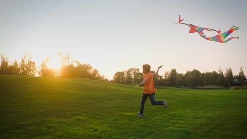Boy Running Across Field While Kite Soaring High Into Sky