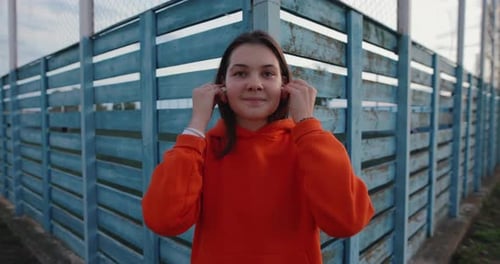 Young Adult Wearing Earbuds by Blue Urban Fence