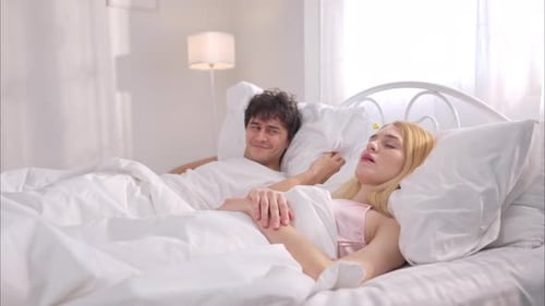 Un jeune homme couvre le nez de sa femme avec les mains tandis que son partenaire ronfle bruyamment à côté de lui dans son lit