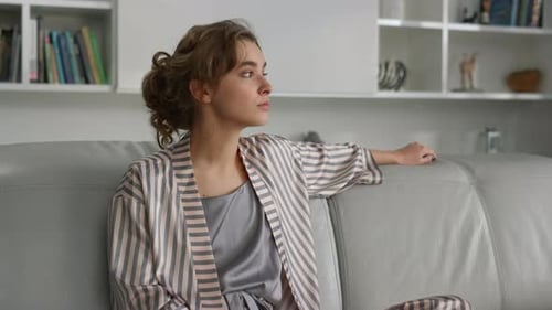 Woman in pajamas sitting on couch looks thoughtful