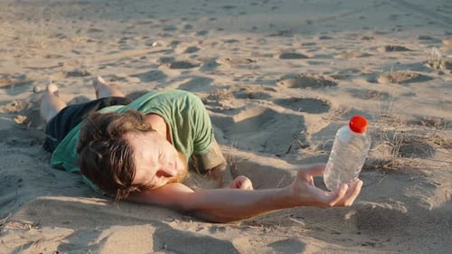 A man lies on the sand under the scorching sun in the desert. He's thirsty, He holds an empty bottle