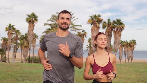 Man and Woman Exercising Outdoors Running Along a Palm Lined Path Taking a Break After an Intense