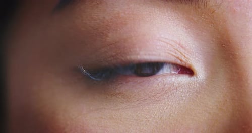 Slow motion macro close up of asian female eye with perfect natural makeup looking and blinking in