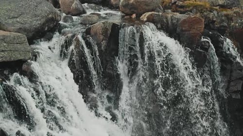 Flusswasser fließt in Zeitlupe einen Wasserfall hinunter und prallt gegen wunderschöne schwarze Felsen