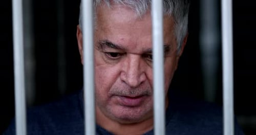 Older man feeling trapped holding into iron gate. Senior holds on bar imprisoned
