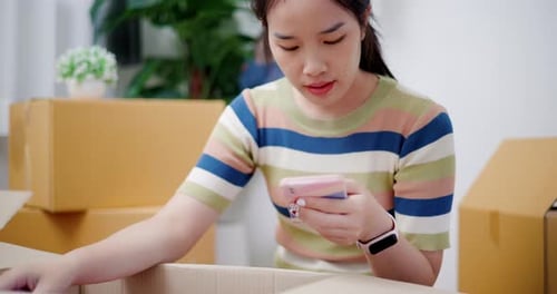 Young Woman Unpacking Box with Smartphone