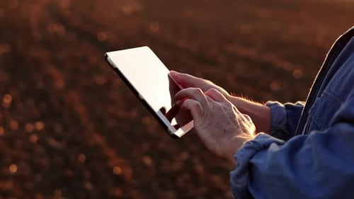 Cropped shot of male farmer's hands use digital tablet on plowed field for control of soil quality,