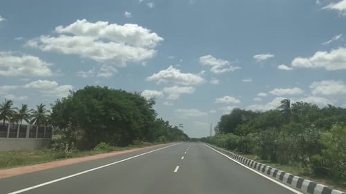 a beautiful view of empty highway with trees and bushes on both side of the roads and a beautiful sk