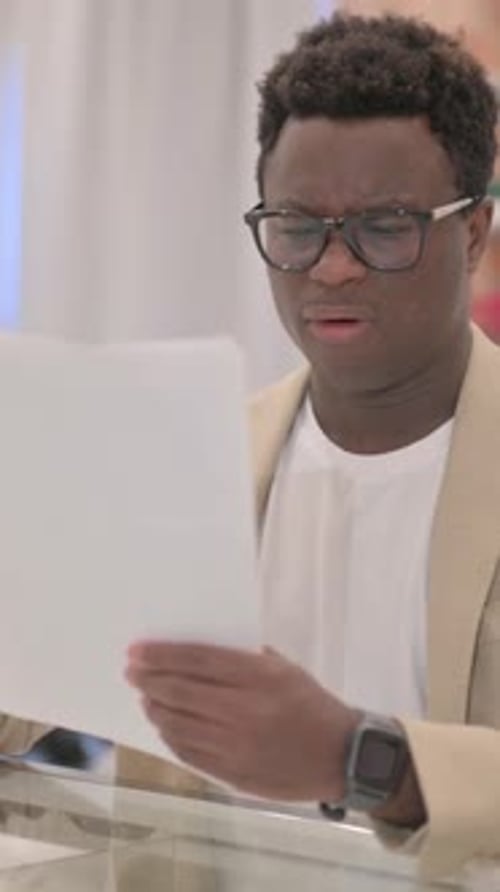 Serious Man Reads Documents Indoors, Reacting Negatively