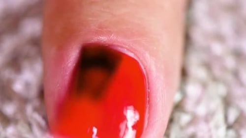 Extreme close-up of the brush applying the red nail polish.