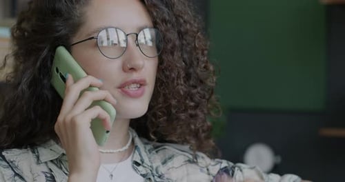 Closeup Portrait of Happy Young Lady Speaking on Mobile Phone and Gesturing Indoors in Office