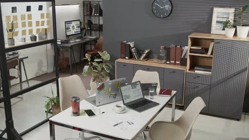 Modern Office Space Showing Rectangular Table with Laptops, Coffee Cup, Thermos