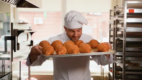Smiling Baker Holding Tray of Fresh Croissants
