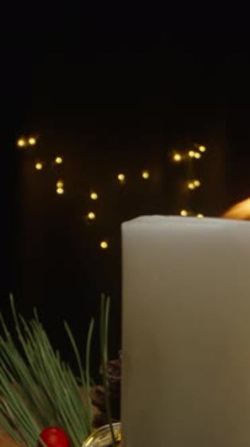 Vertical video. The candle flame flickers from a draft in the dark room adorned with Christmas ornam
