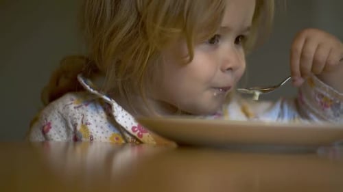 Child Eats Food With Spoon at Table Indoors