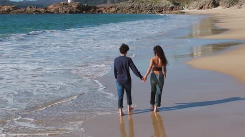 Couple Holding Hands While Walking At The Beach In Summer. - aerial shot