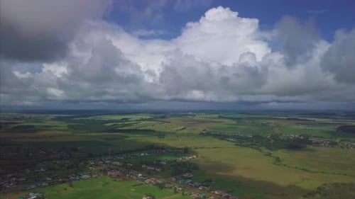 Aerial view of the fluffy clouds at summer sky. Flight over the rural areas with green summer fields