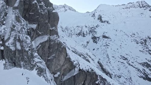 Drohnenaufnahmen, die an einer Klippe in verschneiten Bergen vorbeifliegen.