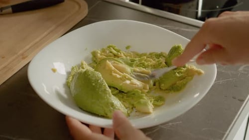 Woman mashing fresh avocado in bowl for guacamole
