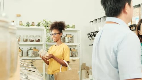 A young woman is shopping in refill store with reusable bag, zero-waste grocery.