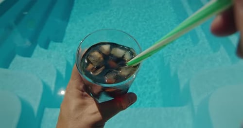 Man Stirring Ice in a Cool Drink with a Pool in the Background Firstperson View