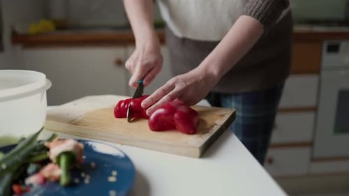 Woman Slices Red Bell Pepper in Kitchen at Home