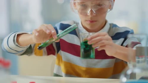 Elementary School Science Classroom: Smart Little Boy wearing Safety Glasses Mixes Chemicals in Bea