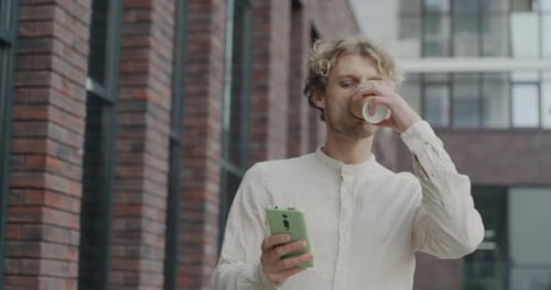 Dolly Shot of Young Businessman Walking in City Street Drinking Take Away Coffee and Using