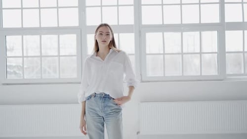 A Woman in Jeans and a White Shirt Stands By a Window