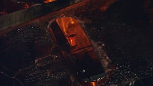 Slow motion of Molten glass pouring out of a Glass melting furnace in a bottle production facility.