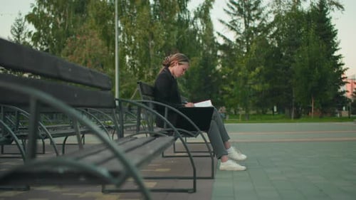 Student Reading Red Folder Outdoors with Laptop in Quiet Park Setting