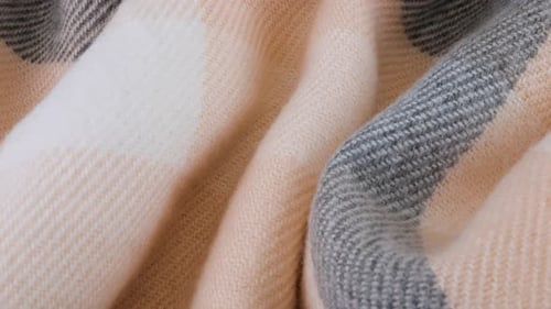 Top view of the soft folds of wool fabric in pastel gray-pink colors rotated on the display case.